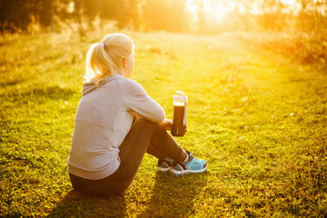 Woman sitting on the grass in the Park with a smoothie.