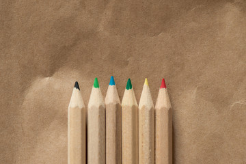 6 colored crayons in a row on beige paper background - text space on top