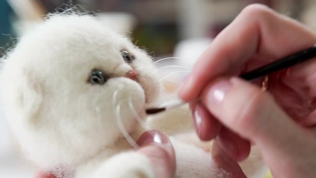 Final touches: the process of drawing a muzzle to a toy kitten from felt. Handmade: the technique of creating woolen toys. Concept hobby, needlework, exclusive work.