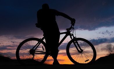 Fototapeta na wymiar Silhouette of cyclist on the background of sunset. Biker with bicycle on the sand during sunrise