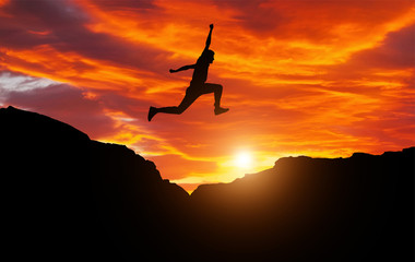 Silhouette of athlete, jumping over rocks in mountain area against sunset. Training running and jumping in difficult conditions in a beautiful nature with cloudy sky