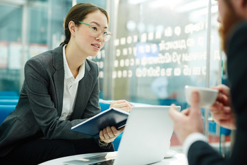 Young woman with notebook talking to colleague at meeting