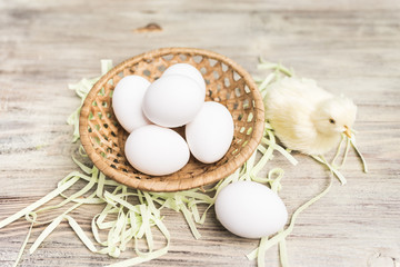 Fototapeta na wymiar Wicker basket with eggs near a young yellow chicken