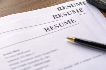 Resume (curriculum vitae, cv) and pen on a written wooden table.