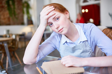 Tired and sad waitress sitting by table after work
