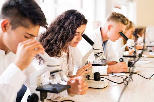 Beautiful high school students with microscopes in laboratory.