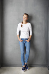Fototapeta na wymiar Full length studio shot of a casual young woman standing at grey wall. 