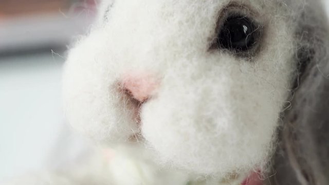 Soft toy of wool (felt) handmade: white-gray rabbit or rabbit as in Alice in Wonderland. Toy on a light background, close-up. The concept of needlework, collectible toys, hobbies. Causes tenderness
