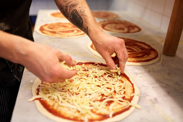 cook adding grated cheese to pizza at pizzeria - obrazy, fototapety, plakaty