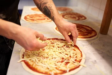 Foto op Aluminium cook adding grated cheese to pizza at pizzeria © Syda Productions