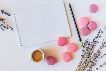Сolorful french macarons, cup of coffee, clean notebook and flowers on white background. Top view, flat style.