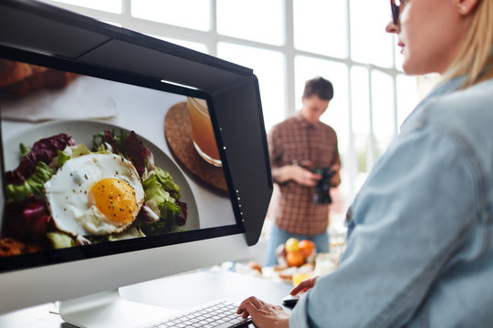 Professional food designer retouching photo while sitting in front of modern computer, spacious production studio with panoramic windows on background