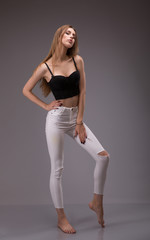Portrait of attractive young, blonde, Caucasian woman in black crop top and white pants posing. Studio shot