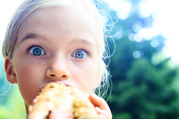 Little child girl eating a hot dog outdoors in summer