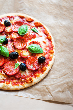 Pepperoni pizza with fresh ingredients on brown baking paper background, top view. Banner or wallpaper .