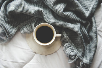 Cozy winter home background, cup of hot coffee with marshmallow, warm knitted sweater on white bed...