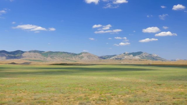 Landscape of steppes and hills on blue sky background, time lapse / Steppe and mountains against blue sky with floating white clouds, time lapse 