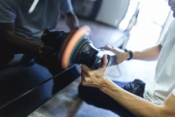 Car detailing - Hands with orbital polisher in auto repair shop. Selective focus.