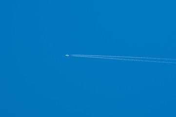 twin engine passenger plane leaves fuel vapor trail in cloudless blue sky
