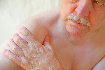 An older man with a hand on an aching shoulder joint