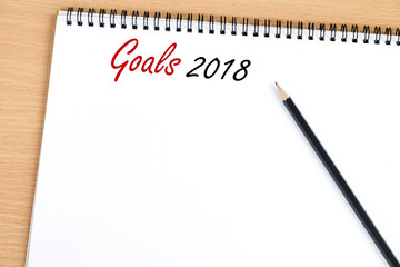 2018 goals on paper note book background on office table, business and new year concept