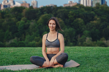 Fototapeta na wymiar Portrait of happy smiling happy slim fit young white Caucasian women sitting on yoga mat in park outside at sunset. Yogi girl having break after workout. Summer outdoor activity
