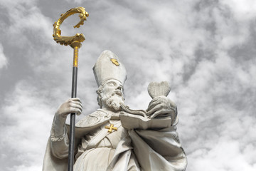 White marble sculpture of Saint Augustine with golden cross and bishop's crook, holding a heart in...
