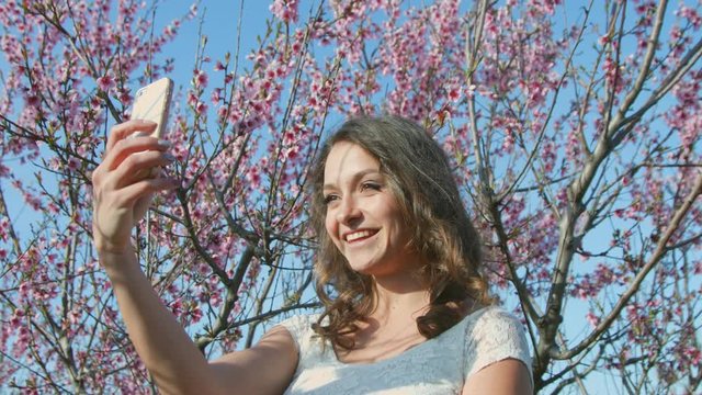 Attractive girl doing selfie on the background of flowering trees