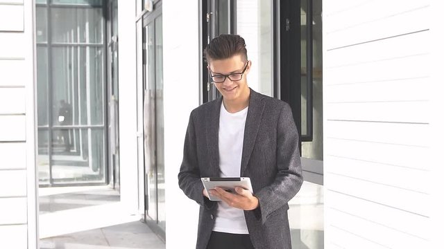 Young businessman uses tablet on background of modern building.