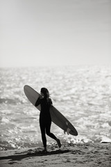 Young woman dressed in a surf suit, holding her board on the beach