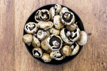 Black bowl on un-cooked mushrroms with wooden background