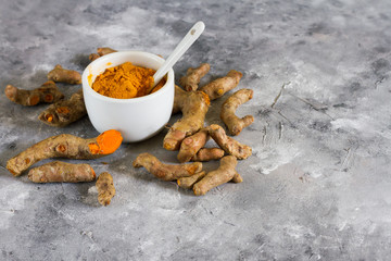 Turmeric root and ground turmeric. White bowl, gray background.