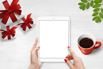 Female hands holding tablet with isolated screen on the table, surrounded with gift boxes, coffee and plant