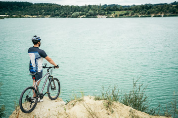 Fototapeta na wymiar man with bicycle stand on the hill and looking at the lake