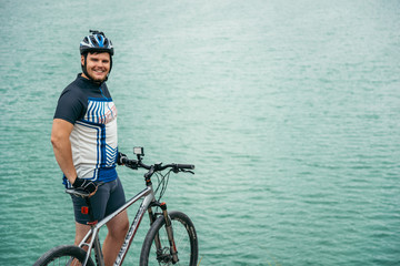 man with bicycle stand on the hill and looking at the lake