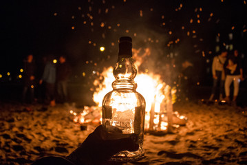 Glass bottle held in front of bon fire