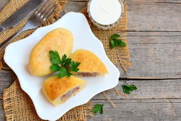 Fried potato zrazy stuffed with a meat on a white plate. Sour cream, fork, knife on a vintage wooden table. Homemade zrazy recipe. Wooden background with copy space for text. Top view