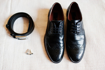 Close-up photo of groom's black shoes, belt and golden cufflinks.