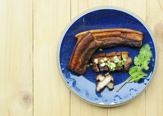 Fried pork belly with fish sauce with green coriander on blue dish on wooden table backgrounds above