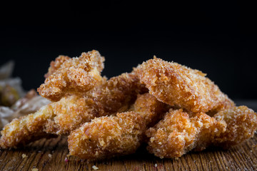 Chicken breast nuggets on wooden background. Pile of crispy homemade baked chicken nuggets cooling. Close up.