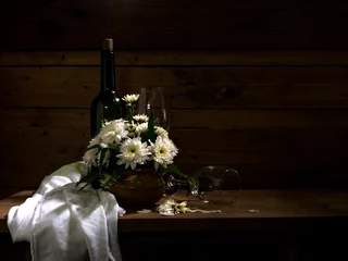 Fotobehang Eetkamer The visual art still life image of a bottle of wine with a empty wineglass and a vast of white flowers on the wooden old table that in the dark room with dim light getting through.  © Mongkolchon