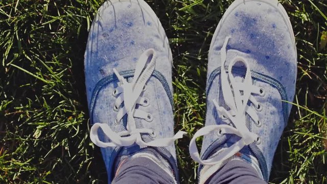 Female feet wears sneakers in blue jeans color sports shoes moving and posing on a sunlit green grass in slow motion. 1920x1080