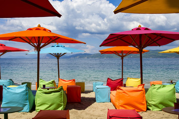 Obraz na płótnie Canvas Modern beach equipped with umbrellas, and multicolored inflatable deckchairs for trendy tourists, Skiathos Greece, at the bottom the sea and a cloudy sky