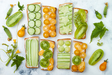 Green and yellow vegetables sandwiches. Variety of sandwiches with cream cheese, cucumbers and tomatoes on a light background. Top view, flat lay, overhead