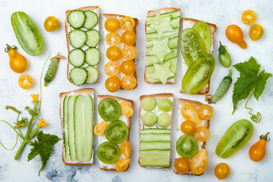 Green and yellow vegetables sandwiches. Variety of sandwiches with cream cheese, cucumbers and tomatoes on a light background. Top view, flat lay, overhead