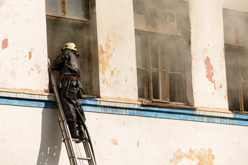 Firefighter training. Fire fighter on ladder in window of house with smoke. Fireman battle with wildfire in building.	