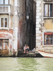 Fototapeta na wymiar Venice, Italy - Circa July 2015: Romantic couple kissing near the Gran Canal in Venice - old buildings around
