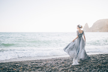 Beautiful brunette girl in long grey winding in the wind dress is made of tulle holds with one hand...