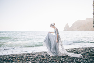 Fototapeta na wymiar Beautiful girl in a long dress with a veil on the beach, summer, rocks