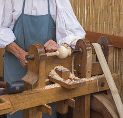 An artisan carves a piece of wood using an old manual lathe